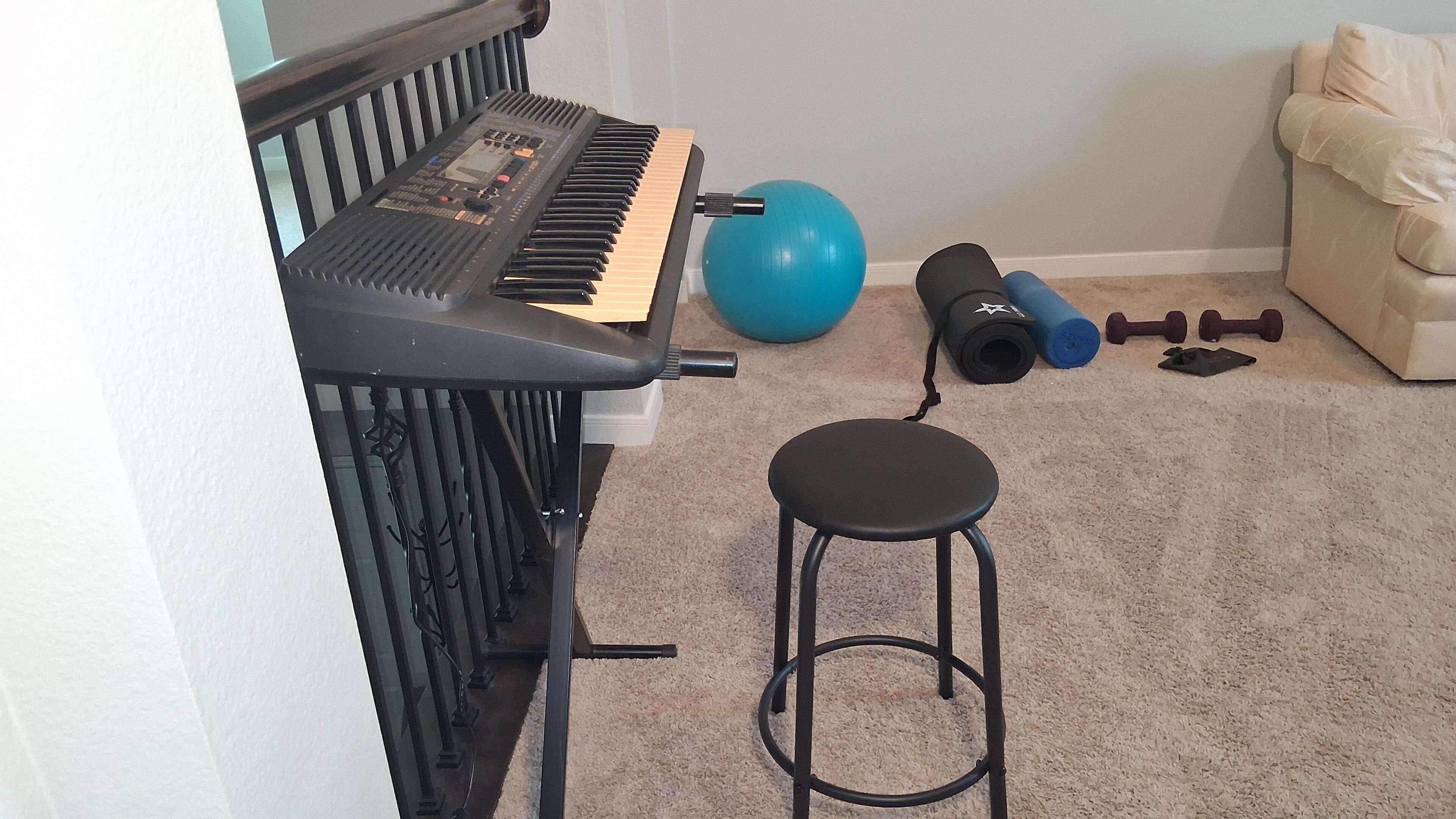 Una habitación con un piano, un balón de ejercicios, mancuernas y un taburete.