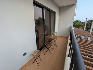 Un balcón con una mesa y sillas de madera, una planta en maceta y vista a la calle.