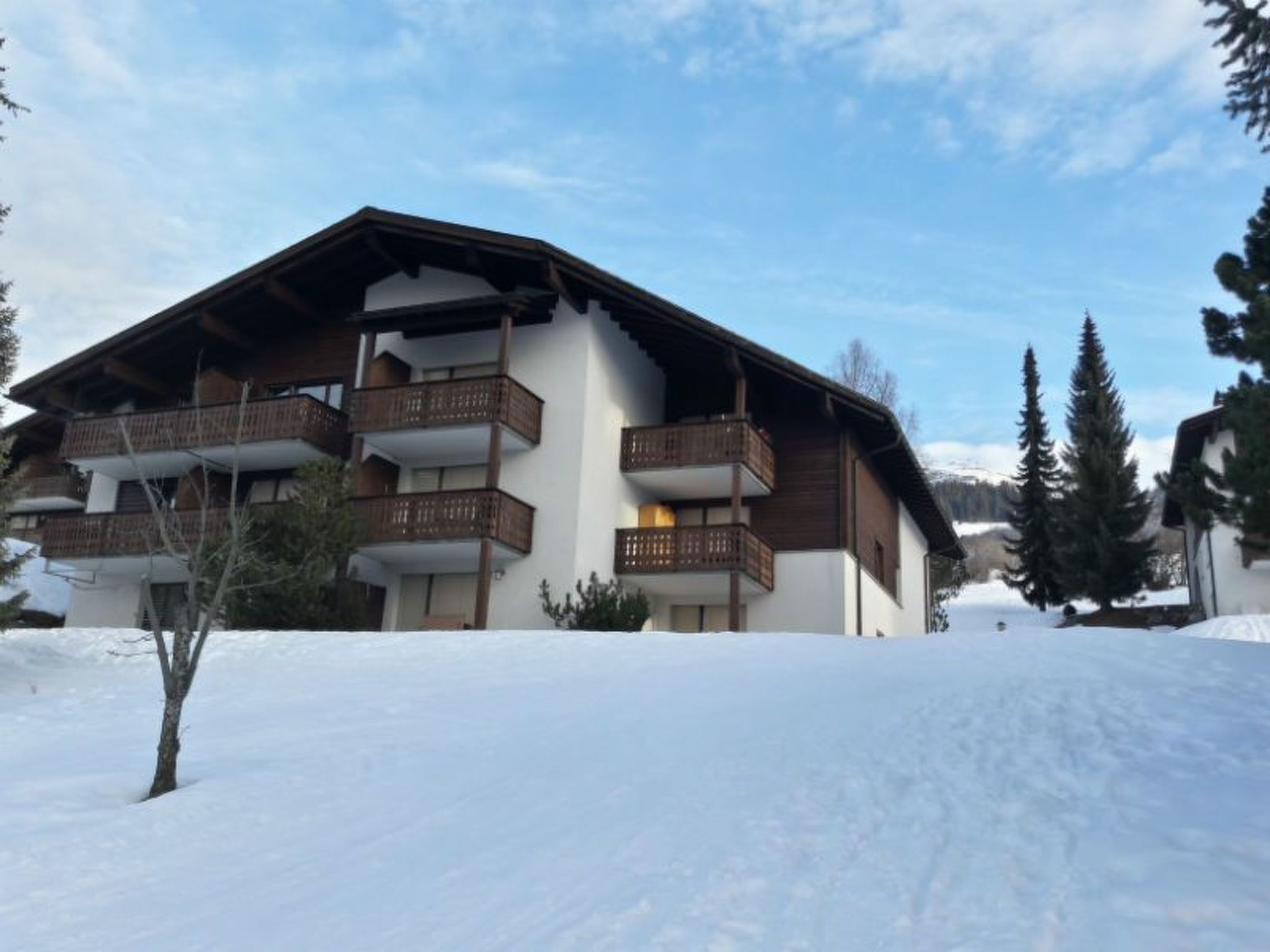 A two-story chalet with wooden balconies, surrounded by snow.