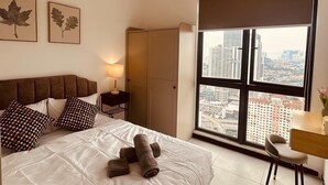 A hotel room with a bed, a ceiling fan, a large window with a city view, and a desk with a chair. - Cozy 2-bedroom apartment near KLCC, TRX, Gleneagles Hospital (Kuala Lumpur)