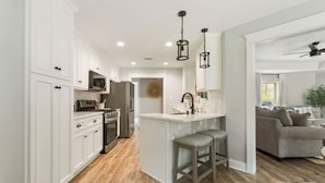 Une cuisine moderne avec des meubles blancs, un îlot central doté de tabourets, un four à micro-ondes et une cuisinière.