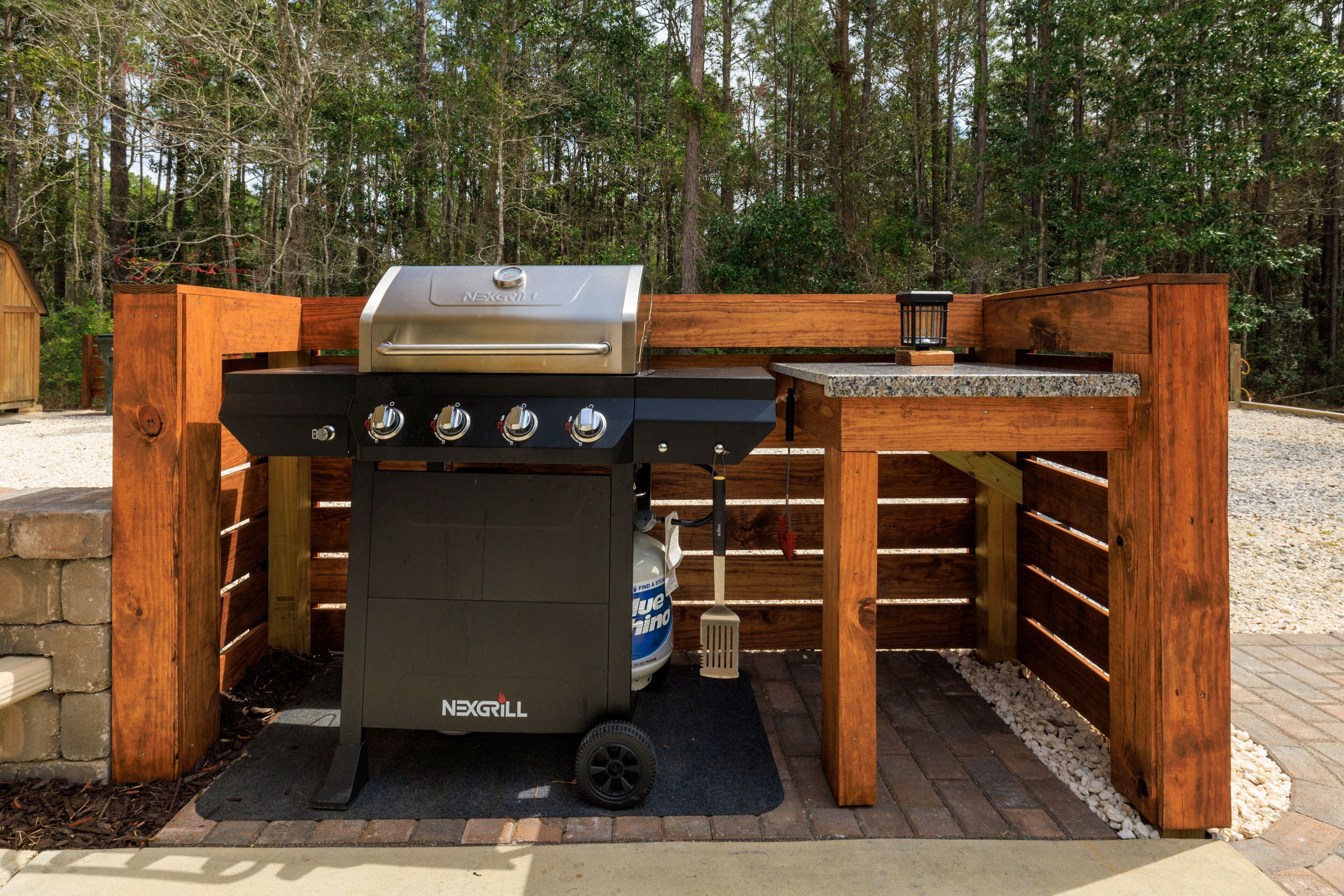 En NEXGRILL-grill med inbyggd kolbehållare, en grill med plan yta och en bänkskiva i sten.