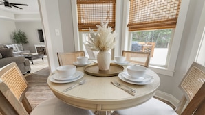 Un coin repas avec une table ronde, des chaises blanches et un vase contenant des fleurs séchées.