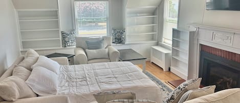 A bedroom with a bed, two armchairs, a small table, a fireplace, and built-in shelving.