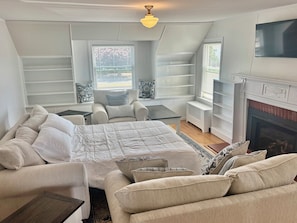 A bedroom with a bed, two armchairs, a small table, a fireplace, and built-in shelving. - Year round 1-bedroom coastal LOFT, sleeps 6, in charming Portsmouth RI (Portsmouth)