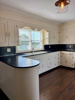 A kitchen with white cabinets, a black countertop, and a window with blinds. - Year round 1-bedroom coastal LOFT, sleeps 6, in charming Portsmouth RI (Portsmouth)