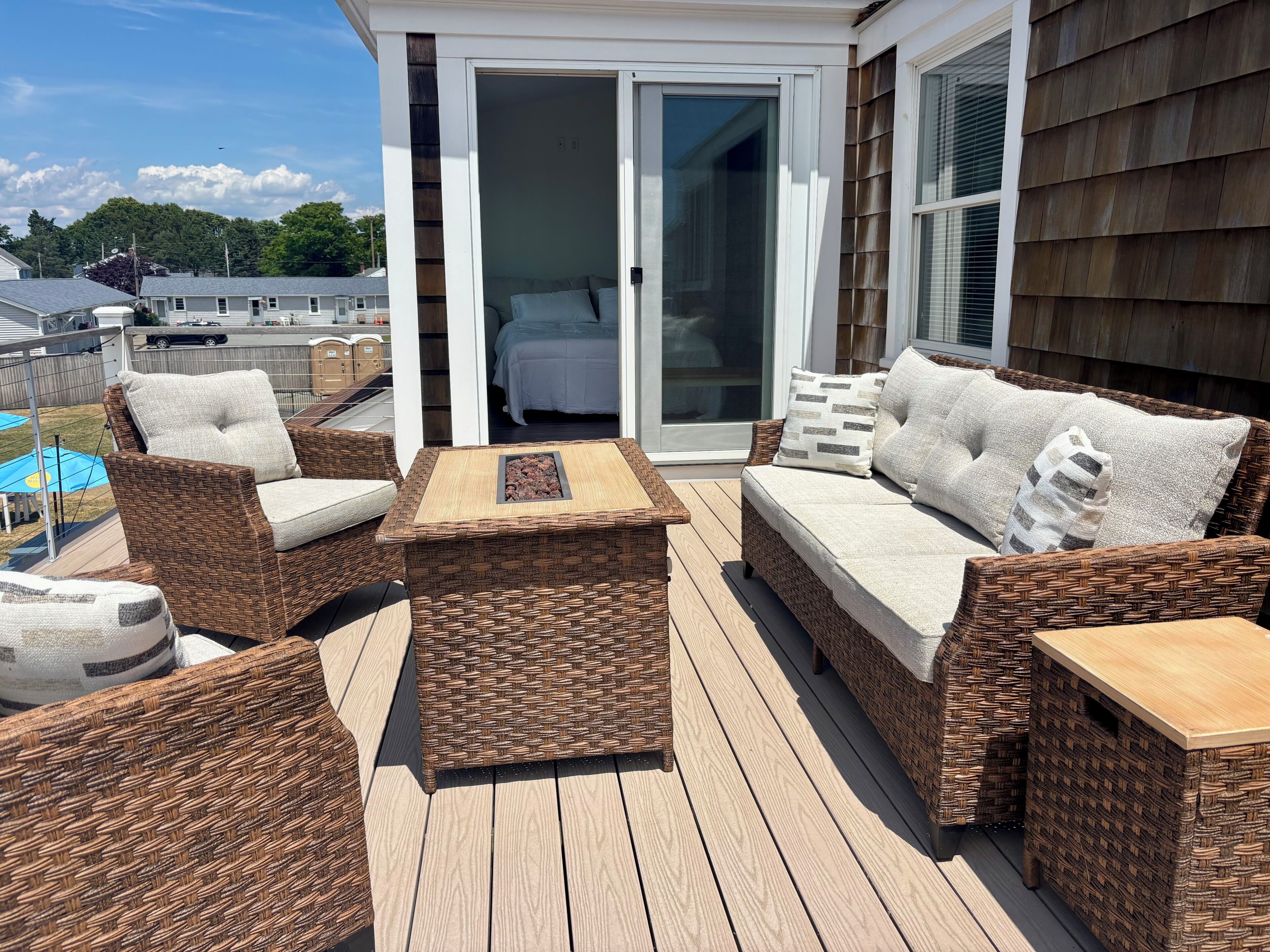 A deck with wicker furniture, a sliding glass door leading to a bedroom, and a view of the neighborhood.