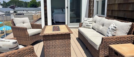 A deck with wicker furniture, a sliding glass door leading to a bedroom, and a view of the neighborhood.