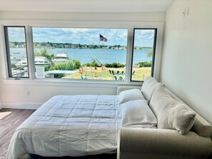 A bedroom with a bed, a sofa, and a large window with a view of a lake and boats. - Year round 1-bedroom coastal LOFT, sleeps 6, in charming Portsmouth RI (Portsmouth)