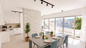 Een moderne keuken met witte kasten, een eethoek met een tafel voor vier personen, en grote ramen met uitzicht op de stad.