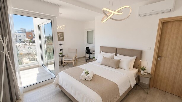 Een moderne slaapkamer met een groot bed, een bureau, een stoel, een klein tafeltje en een deur.