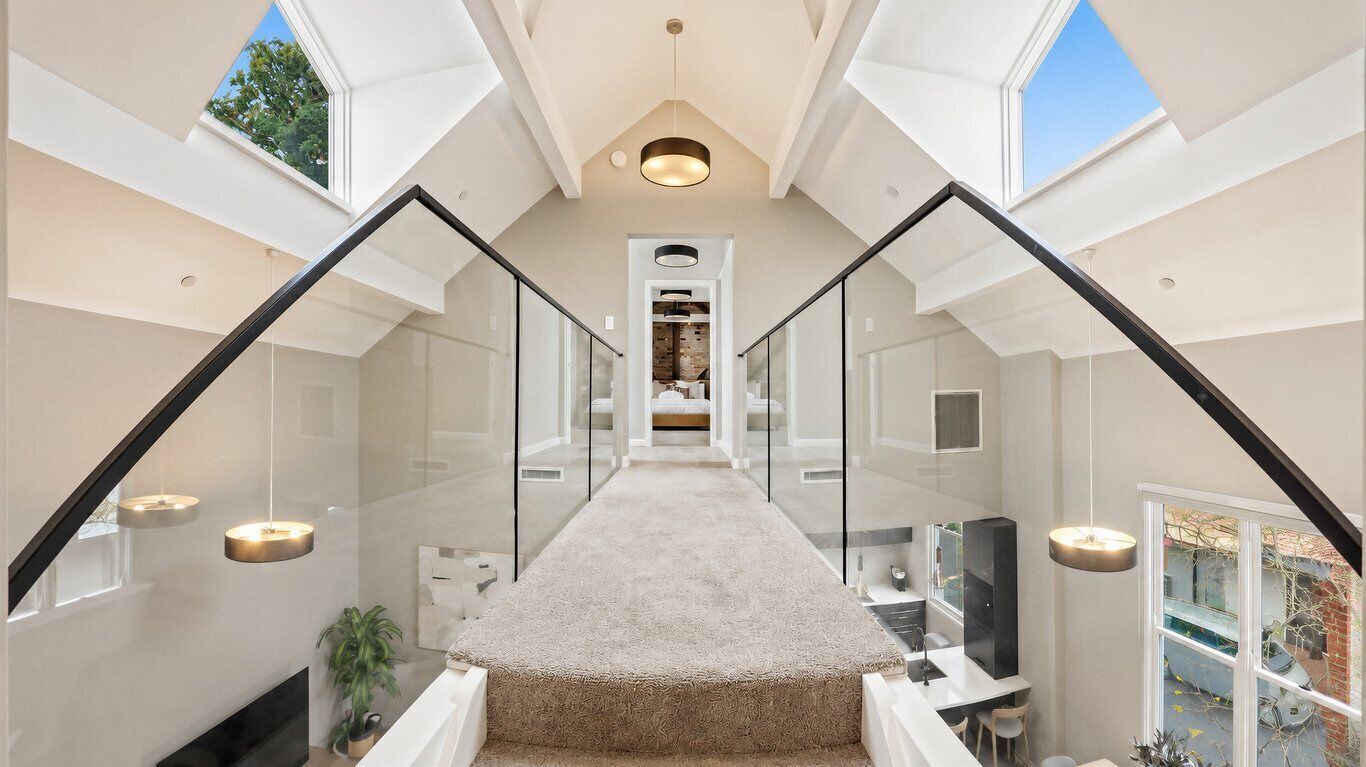 A modern interior with a central staircase, glass railings, and a view through the windows.