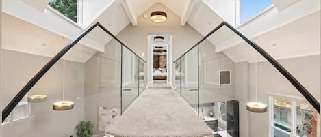 A modern interior with a central staircase, glass railings, and a view through the windows.