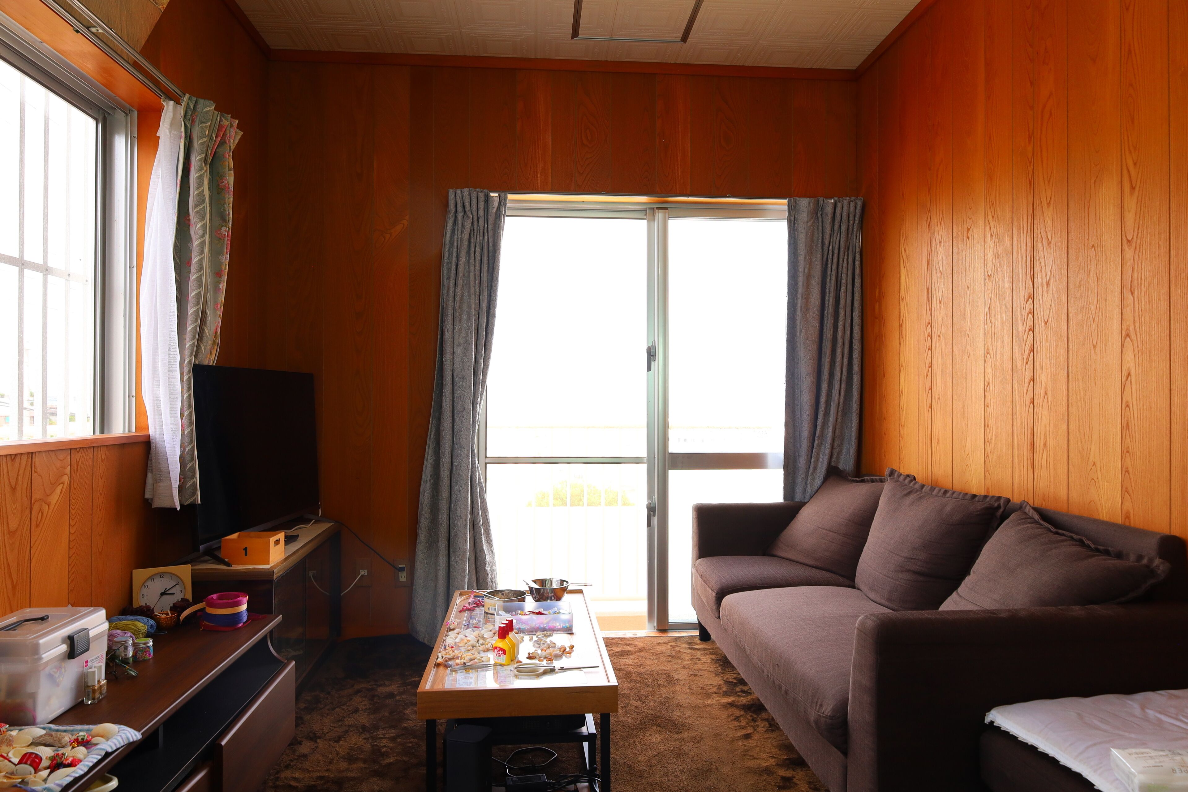 Una habitación con pared revestida de madera, un sofá, una mesa con varios objetos, un televisor y una puerta corrediza de vidrio.