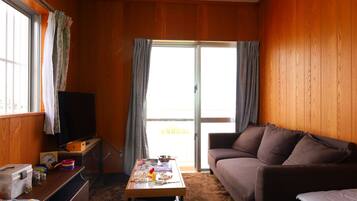 Una habitación con pared revestida de madera, un sofá, una mesa con varios objetos, un televisor y una puerta corrediza de vidrio.