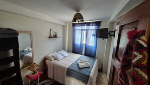 A bedroom with a bed, a bedside table, a mirror, a television, and a door with a colorful curtain. - Charming 1-bedroom apartment in the heart of Cusco (Cusco)