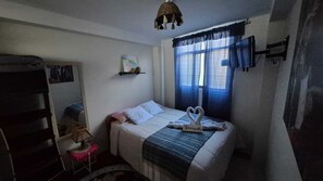 A bedroom with a bed, a bedside table, a shelf with a picture, and a window with curtains. - Charming 1-bedroom apartment in the heart of Cusco (Cusco)