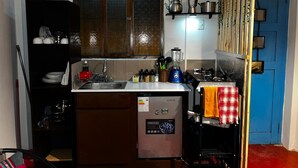 A compact kitchen with a dishwasher, a stove, and a sink. There are shelves above the stove holding pots and pans. - Charming 1-bedroom apartment in the heart of Cusco (Cusco)