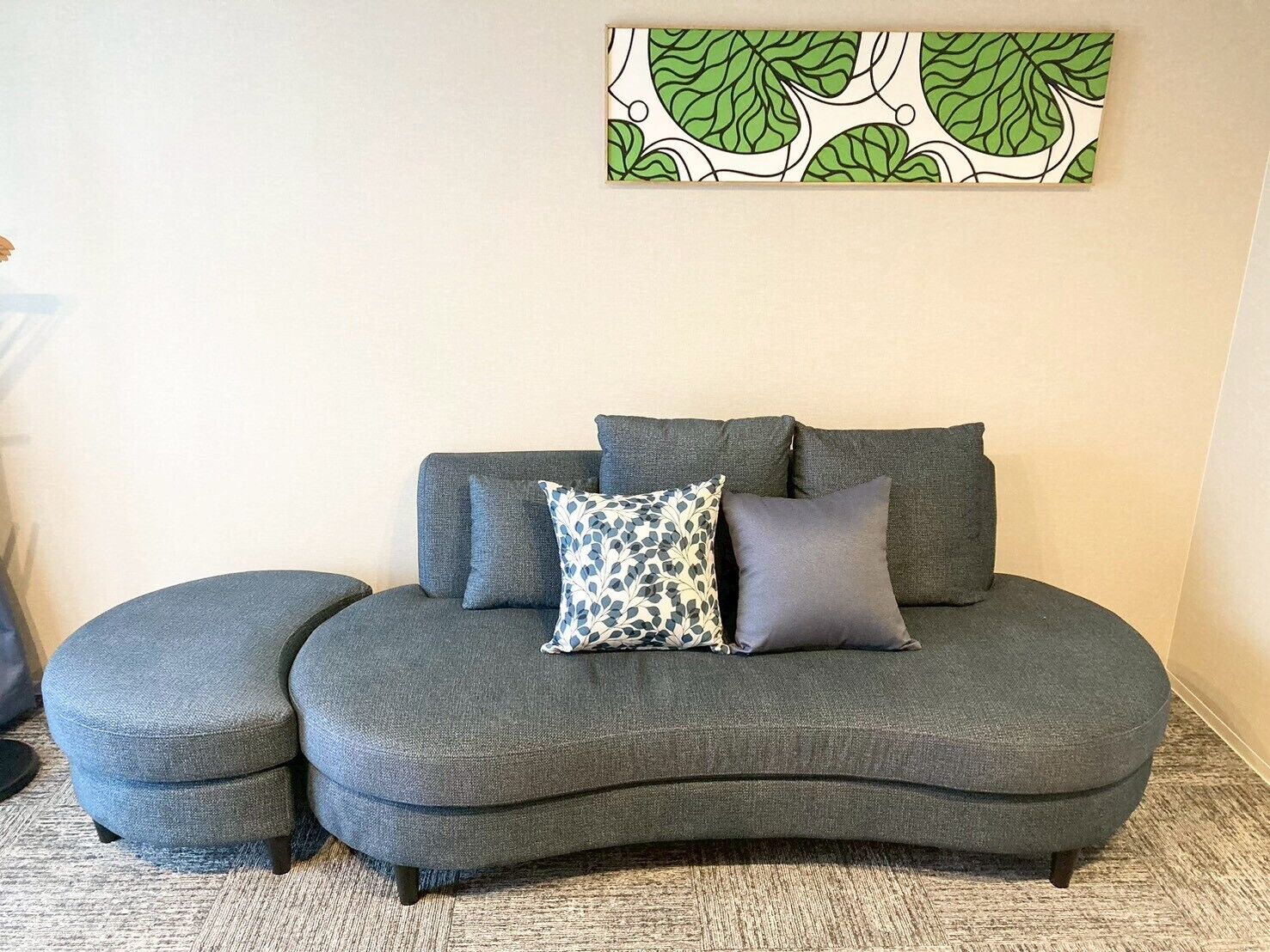 A grey sectional sofa with two matching ottomans, a patterned throw pillow, and a wall art piece.
