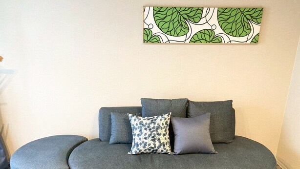 A grey sectional sofa with two matching ottomans, a patterned throw pillow, and a wall art piece. - Koti Sopo Universal Bay 5 by Liaison (Osaka)