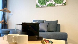 A living room with a sofa, a coffee table with mugs and a small decorative item, and a wall with a leaf pattern. - Koti Sopo Universal Bay 5 by Liaison (Osaka)