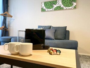 Ein Wohnzimmer mit einer Couch, einem Couchtisch mit Tassen und einem kleinen dekorativen Gegenstand, sowie einer Wand mit einem Blattmuster.