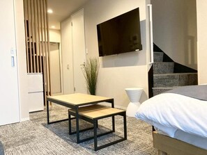 Une chambre à coucher moderne avec un lit, un téléviseur fixé au mur, une petite table et un escalier.