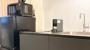 A modern kitchen with a black refrigerator, a coffee machine, and a sink. - Koti Sopo Universal Bay 5 by Liaison (Osaka)