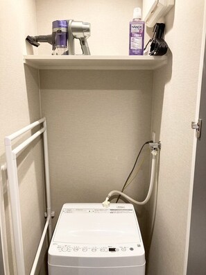 Une petite salle de bain avec un radiateur blanc, un sèche-cheveux et une bouteille de shampoing posée sur une étagère.