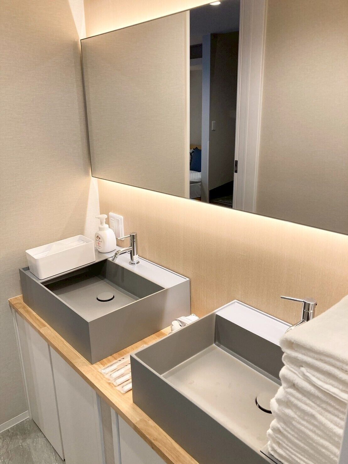 A modern bathroom with two sinks, a mirror, and a wooden vanity.