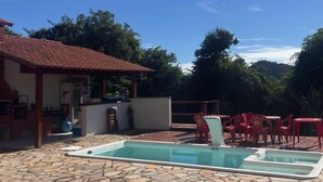 A pool with stone tiles, a barbecue area, and red plastic chairs labeled 'PETRA'. - Green House Lodging Paraty (Paraty)