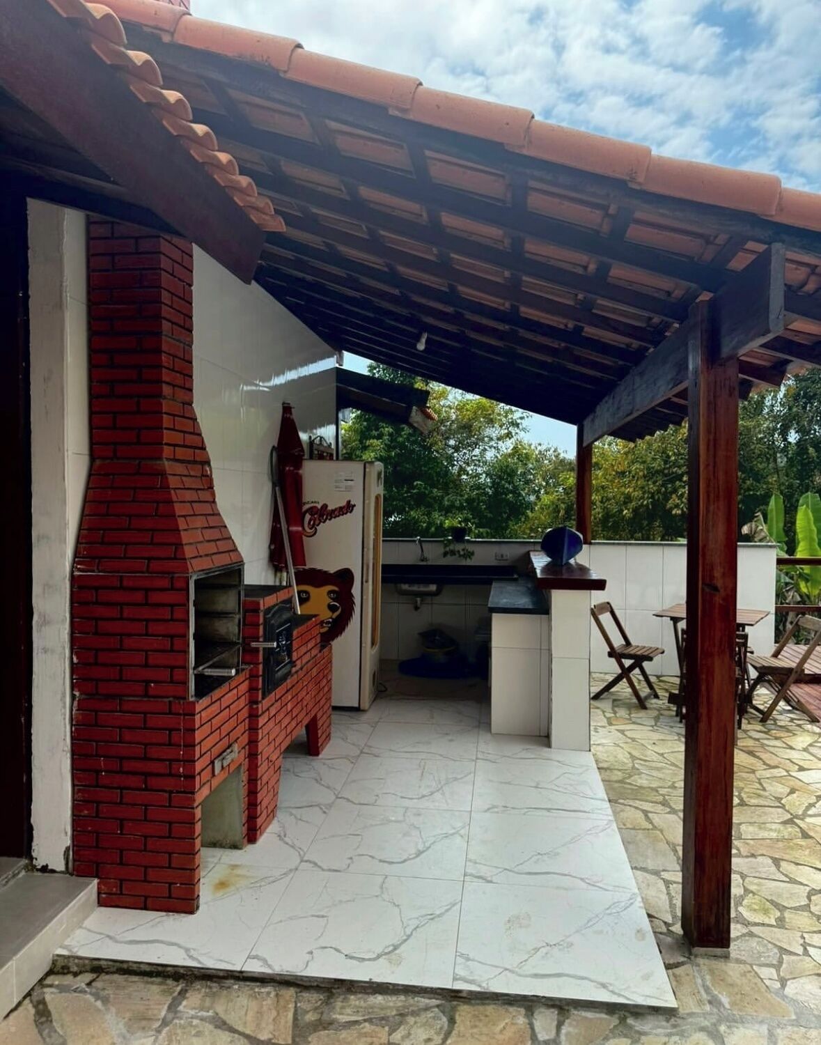 An outdoor patio with a brick grill, a refrigerator, and a table with chairs.