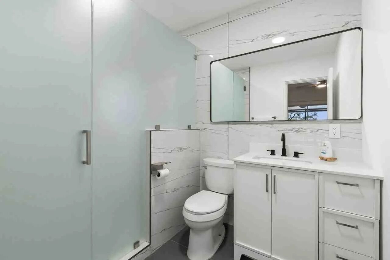 A modern bathroom with a glass shower enclosure, a toilet, a sink with a mirror, and a cabinet.