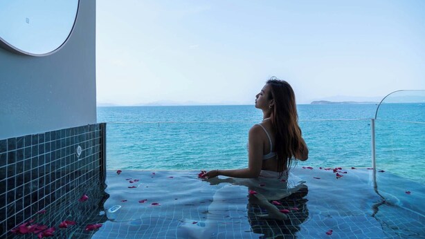 Una persona sentada junto a una piscina con vista al mar.