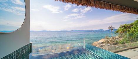 A glass infinity pool with a view of the sea and distant mountains.