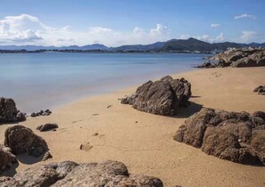 Una playa con rocas grandes, agua tranquila y montañas a lo lejos.