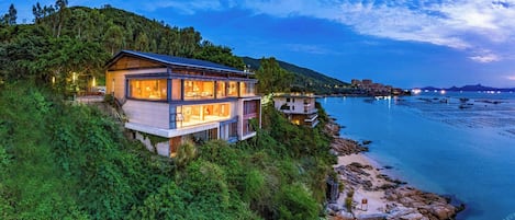 A modern two-story house with a balcony overlooking a coastal area.