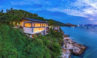 A modern two-story house with a balcony overlooking a coastal area.