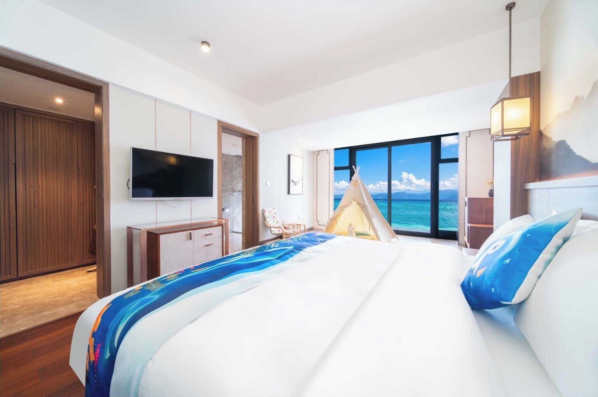 Ein modernes Hotelzimmer mit einem großen Bett, einem Fernseher, einem Kleiderschrank und Blick auf das Meer.