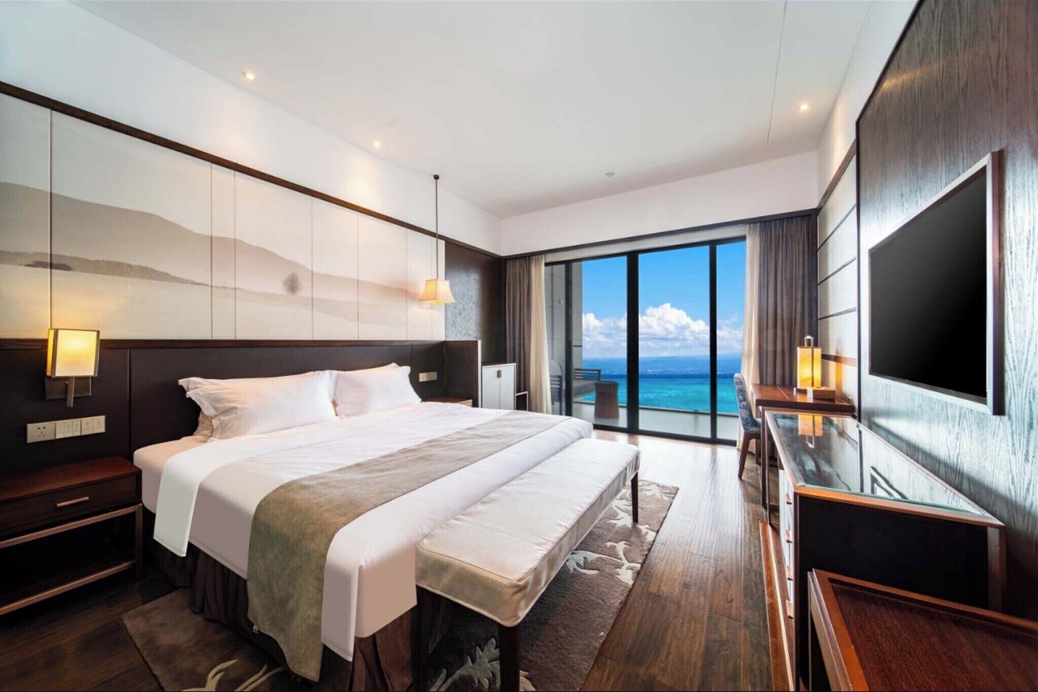 A modern hotel room with a large bed, a TV, and a balcony with a view of the ocean.