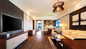 Habitación de hotel moderna con una televisión de pantalla plana grande, un sofá, un comedor y vista al océano.