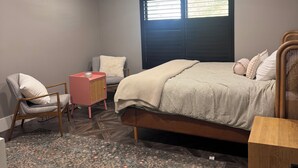 Quarto com cama, uma cadeira, uma mesinha, ventoinha no teto e janela com persianas.