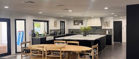 Una cucina moderna con isola centrale, zona pranzo con tavolo e sedie in legno, e soggiorno con divano in pelle e tavolino in vetro.