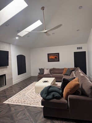 A modern living room with a sectional sofa, a coffee table, a fireplace, and a ceiling fan. - Spacious and beautifully appointed designer 7-bedroom house in Paradise Valley (Paradise Valley)