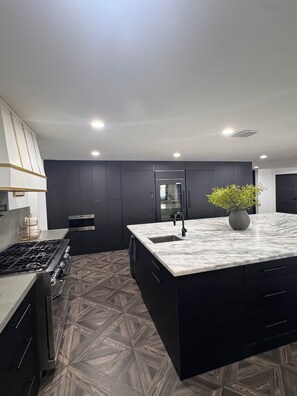 A modern kitchen with dark cabinetry, a marble countertop, a gas stove, and a potted plant. - Spacious and beautifully appointed designer 7-bedroom house in Paradise Valley (Paradise Valley)