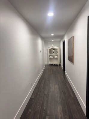 Um corredor com piso de madeira escura, paredes brancas, um armário embutido branco com toalhas dobradas e um quadro na parede.