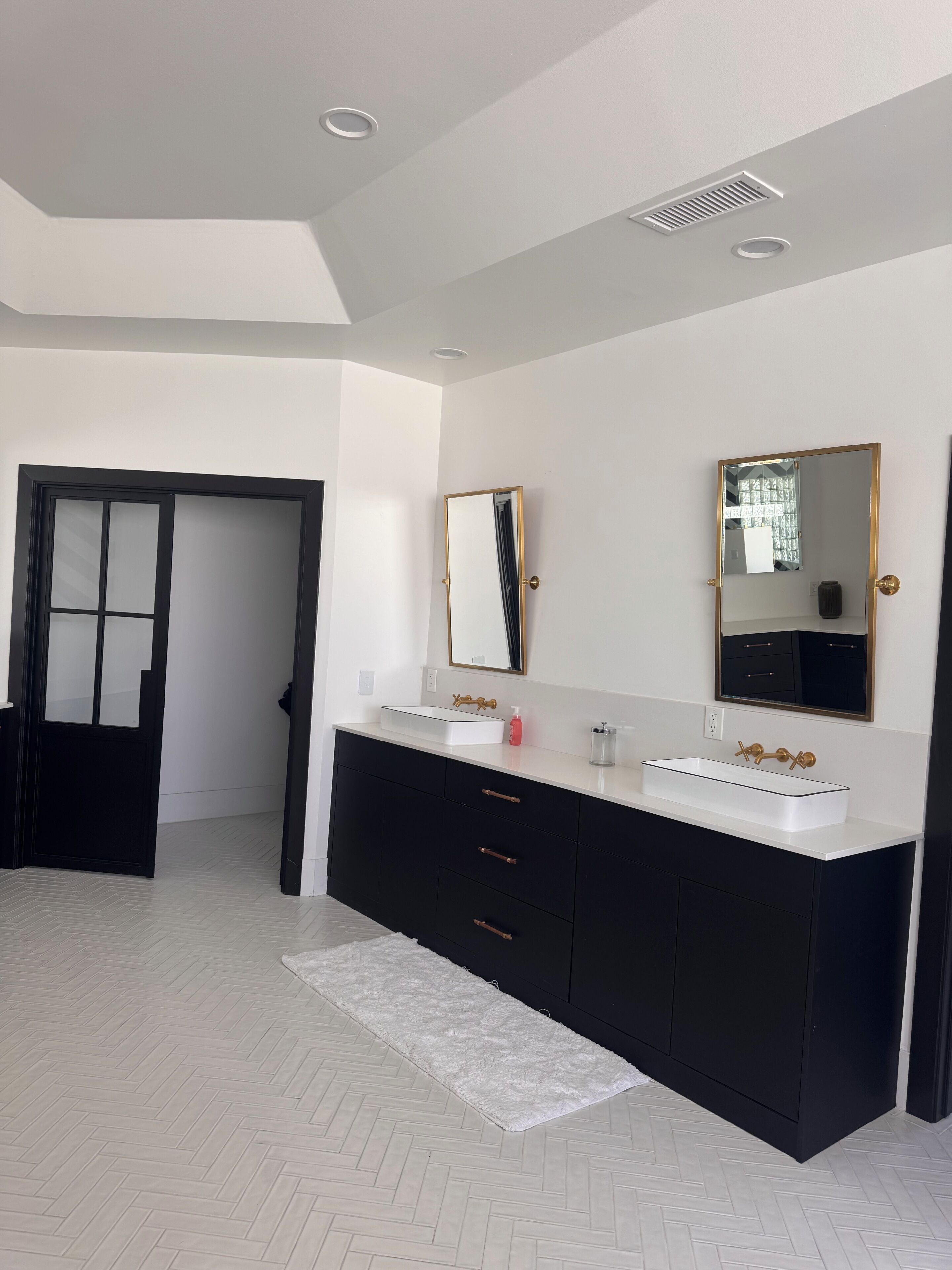 Une salle de bain moderne avec un grand meuble-lavabo, deux vasques, un miroir et une porte.