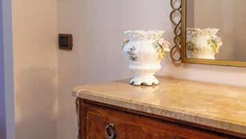 A white ceramic vase with floral designs on a marble countertop, a wooden dresser with a mirror, and a wall switch.