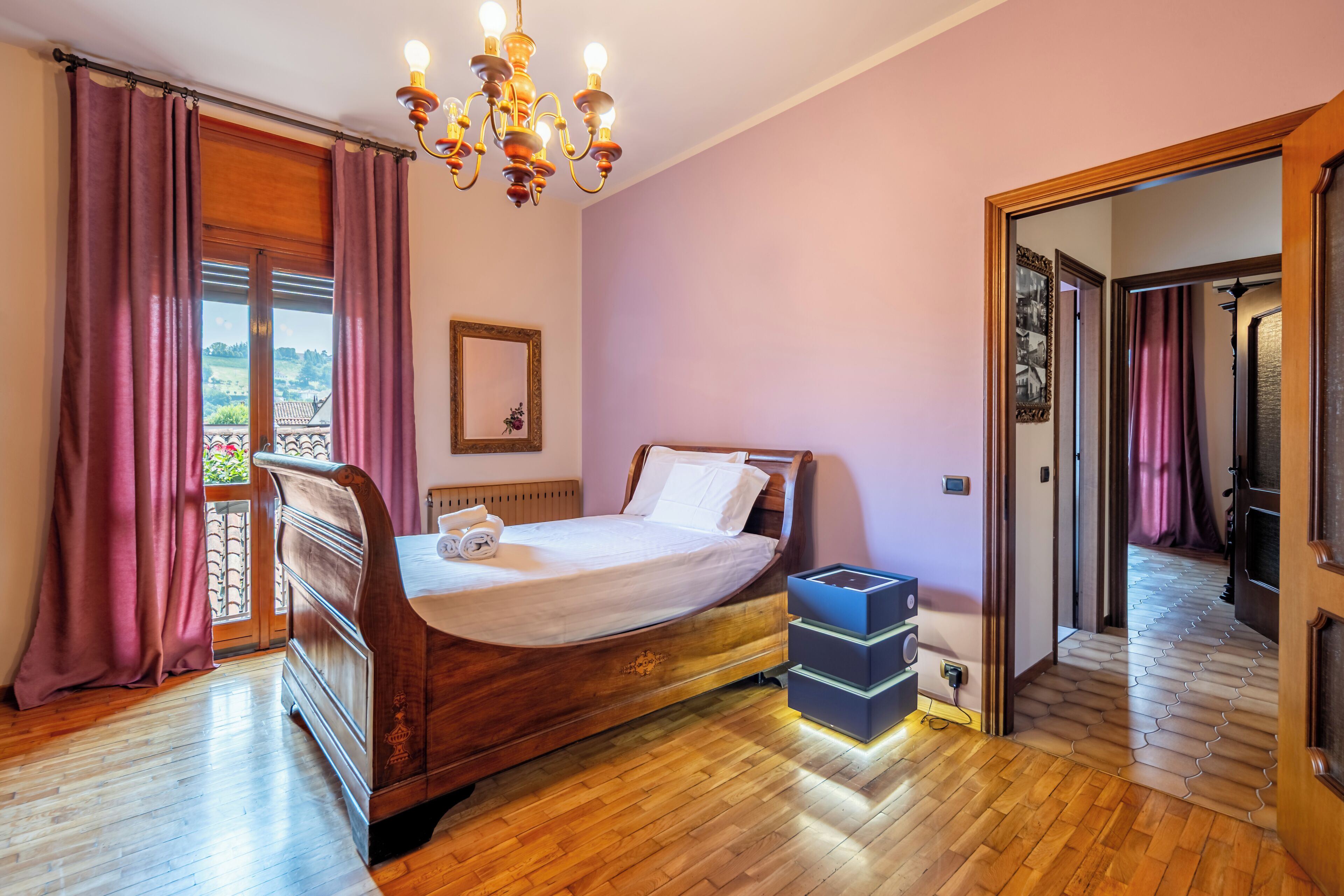 Un dormitorio con una cama de madera, una araña de techo, una ventana con cortinas y vistas al exterior.