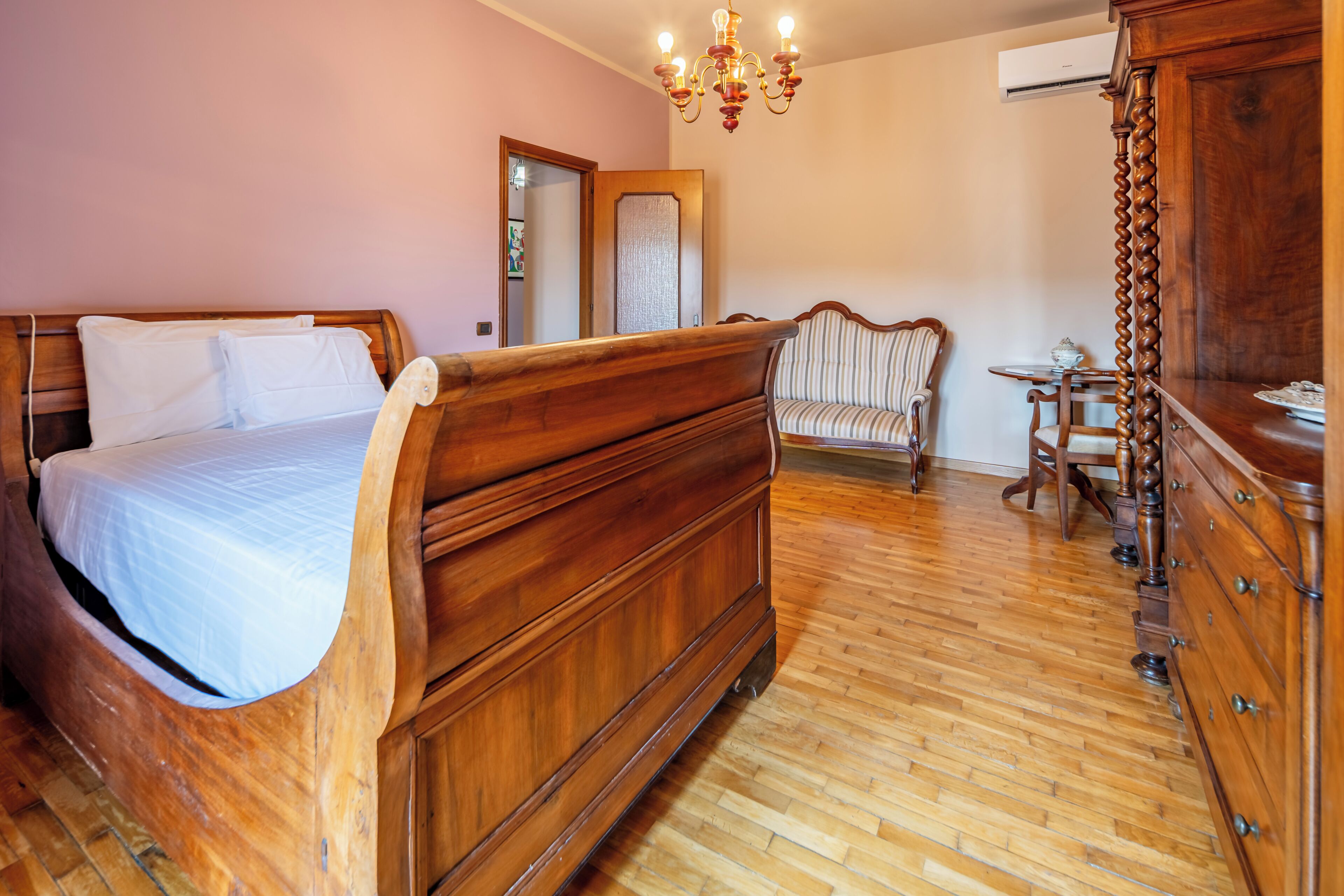 A bedroom with a wooden bed, a chair, a dresser, and a chandelier.